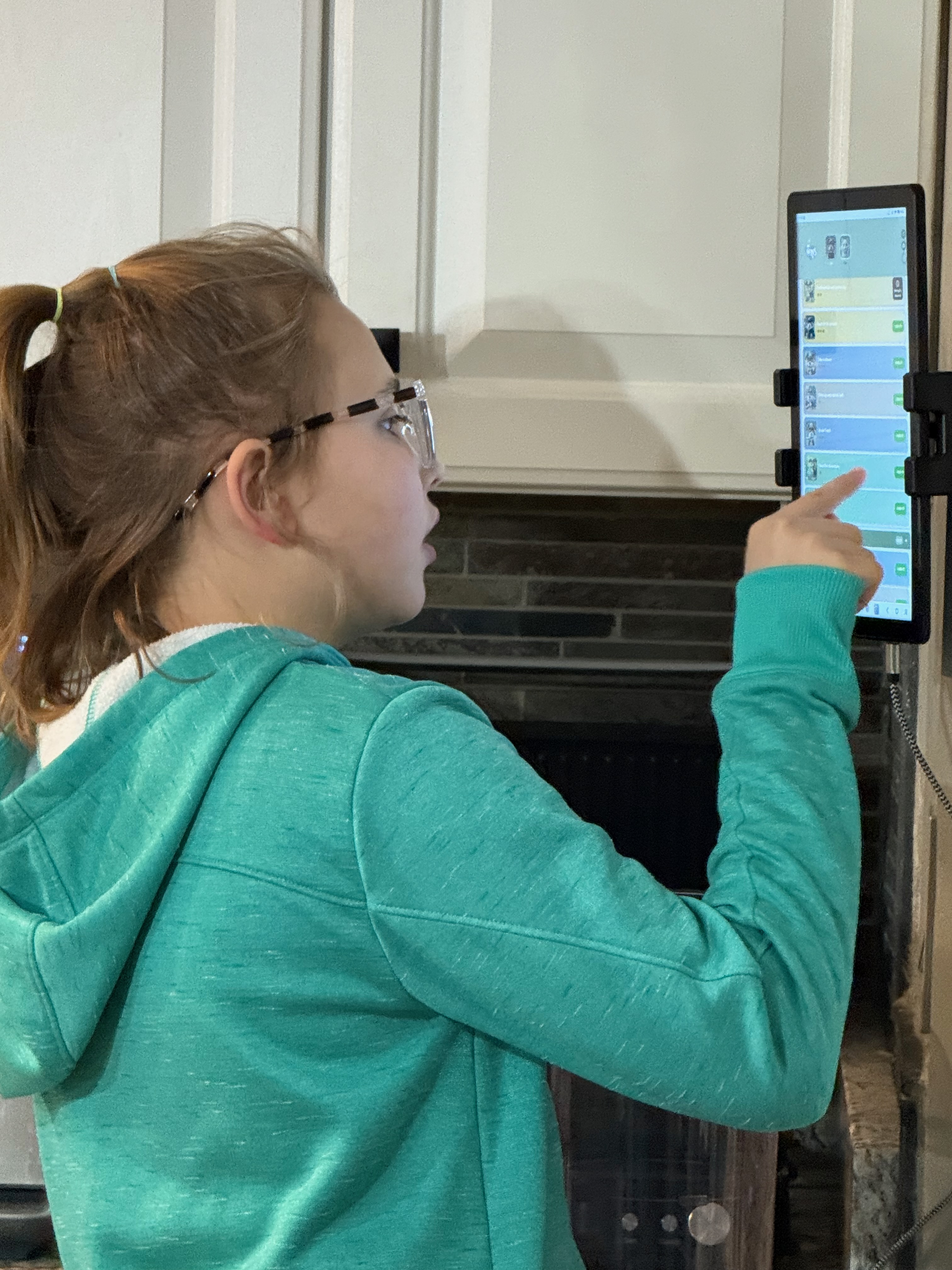 Girl using MyWins chore app on a wall-mounted tablet in the kitchen